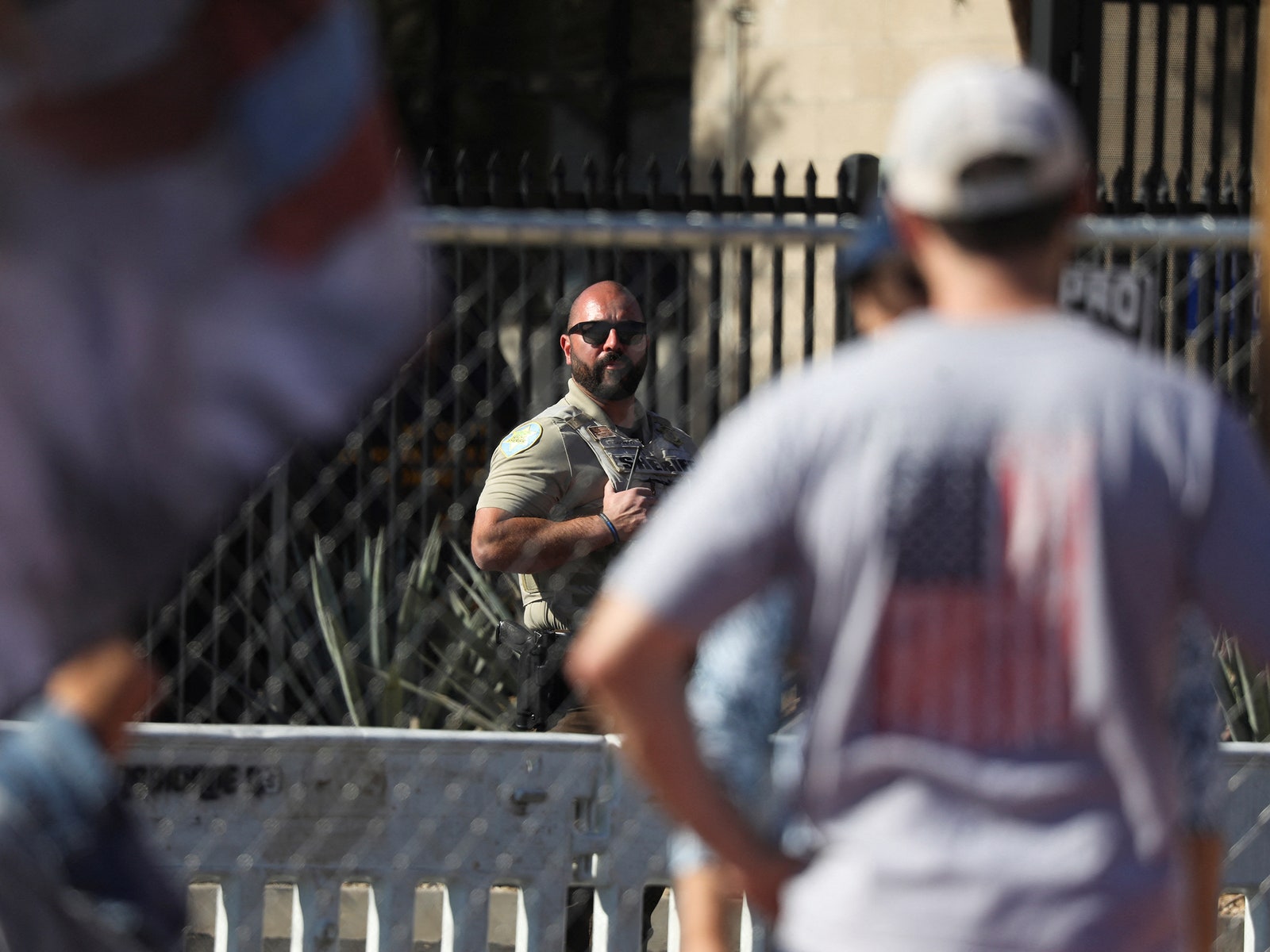 A law enforcement officer keeps watch on demonstrators outside the perimeter of a temporary security fence as they...