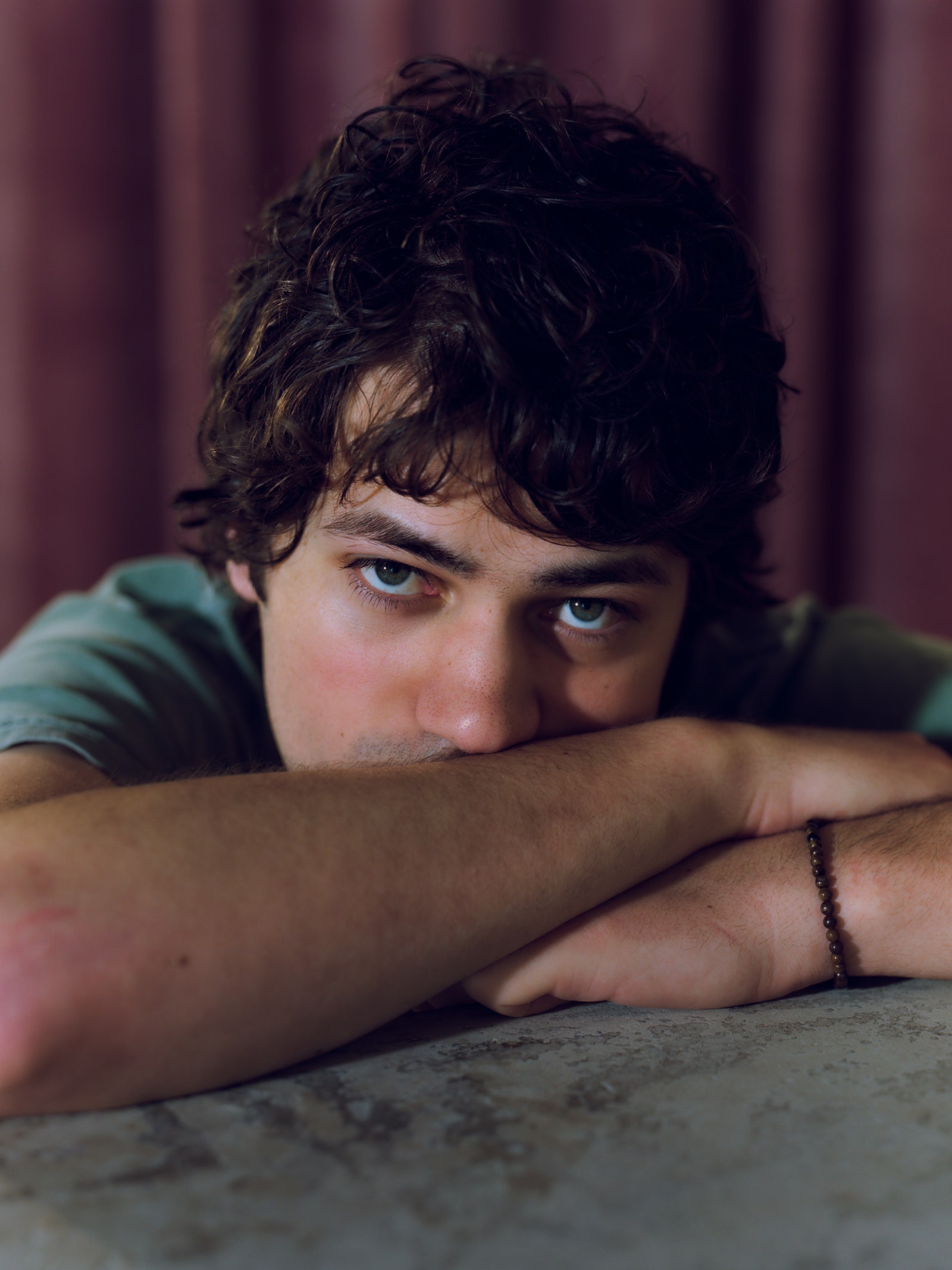 A closeup portrait of MJ Lenderman in a green tshirt resting his head on his arms.